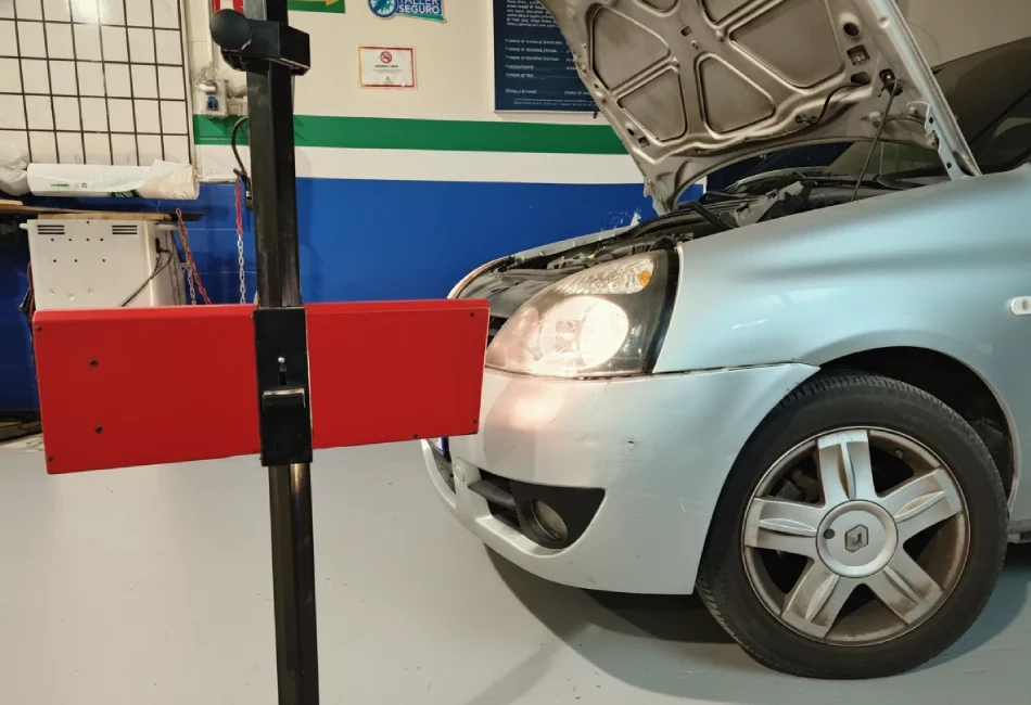 Vehículo plateado con el capó abierto en un taller, siendo revisado con un regloscopio o aparato de ajuste de faros de color rojo